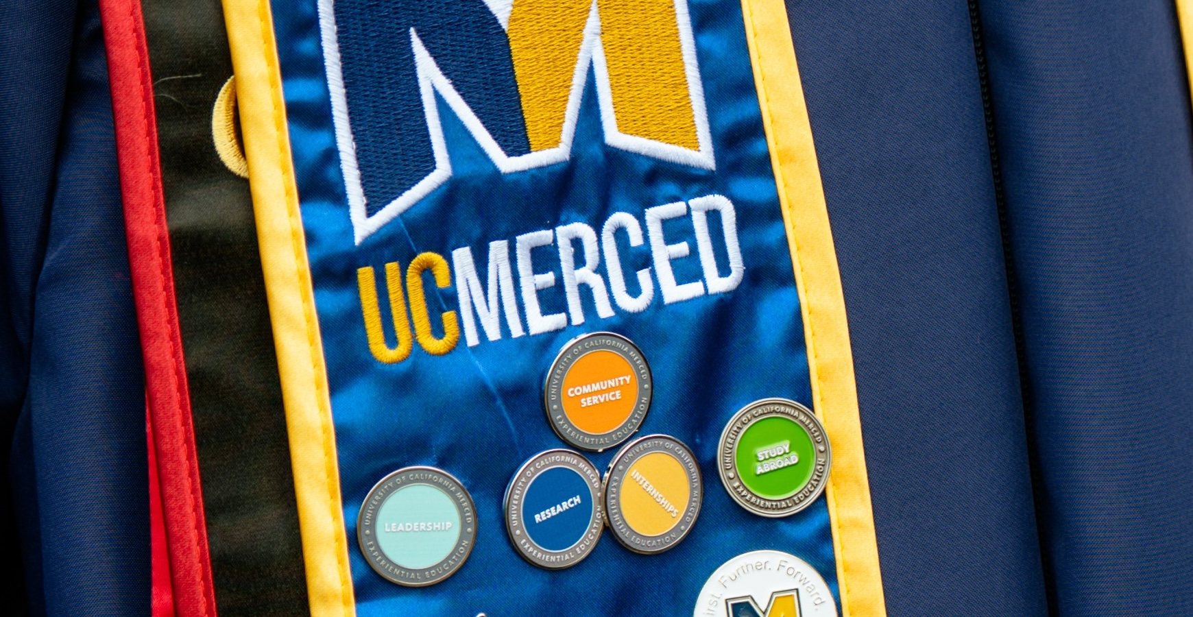 Assorted Experiential Learning pins—including Study Abroad—on a UC Merced graduation stole