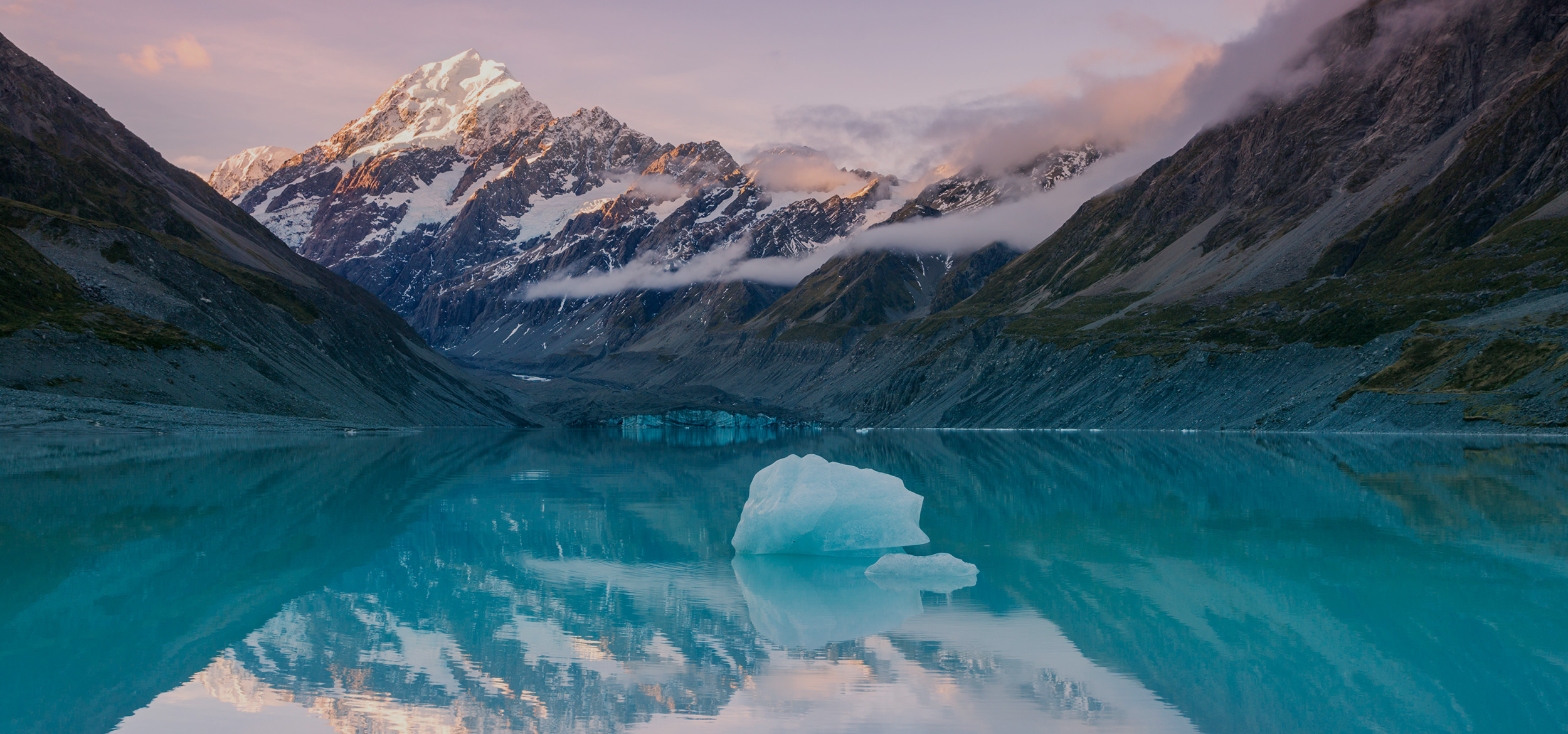 At sunset, the snowcapped peak of Mount Cook reflects in a still lake in a national park of New Zealand’s South Island